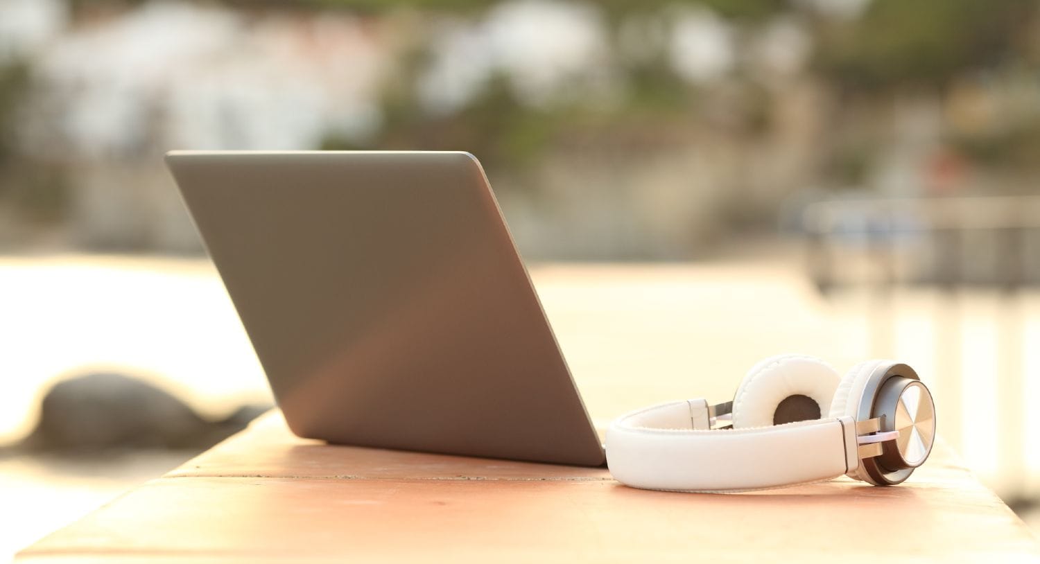 Bærbar computer og hvide hovedtelefoner liggende på en bænk i en park