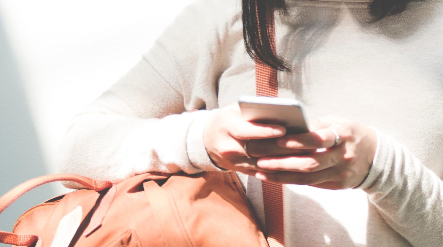 Kvinde med brun lædertaske og hvid bluse anvender iPhone