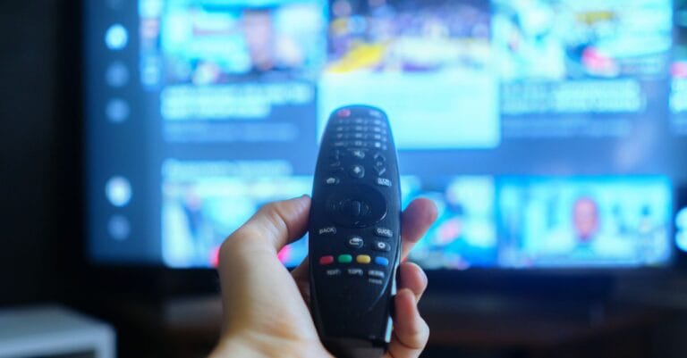 Mand holder fjernbetjening i hånden med fladskærm i baggrunden