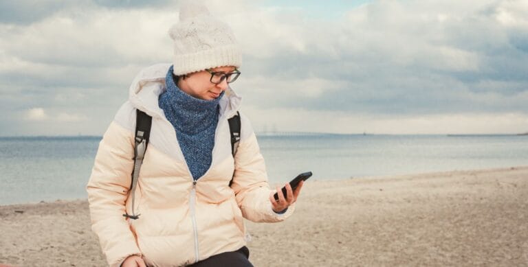 Kvinde på strand tjekker sin mobiltelefon med Storebæltsbroen i baggrunden