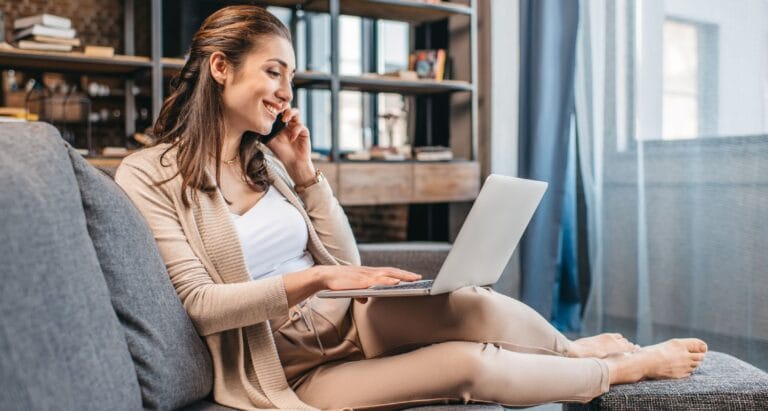 Kvinde med telefon og computer sidder i sofaen i sin stue