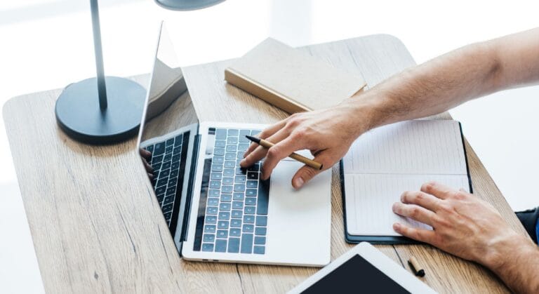 Mand surfer på nettet med Macbook, mens han tager noter i en bog