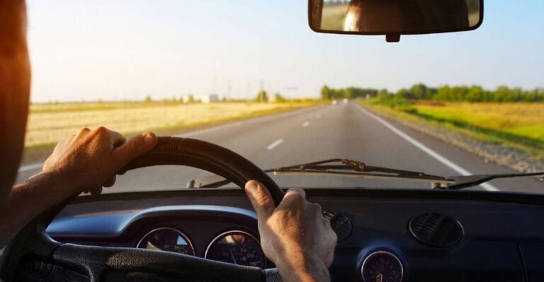 Mand kører bil mellem marker, med sol og blå himmel